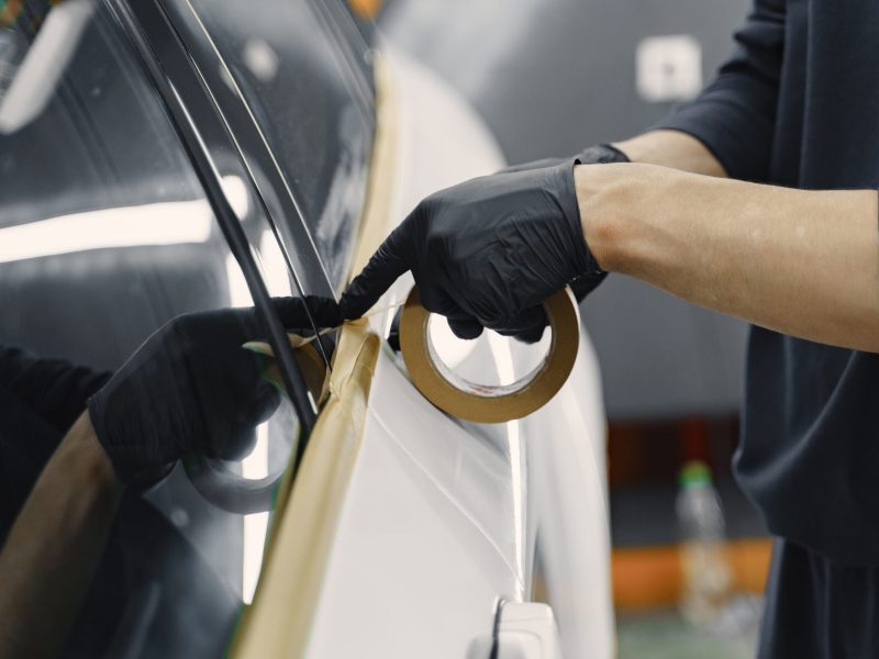 Preparing a car before spray painting Auto body repair series. Masking car before repaint. Man in a black uniform.
